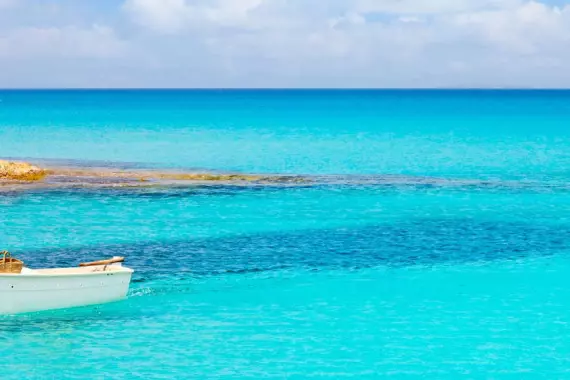 A boat floats on the crystal clear sea in Formentera, Spain.